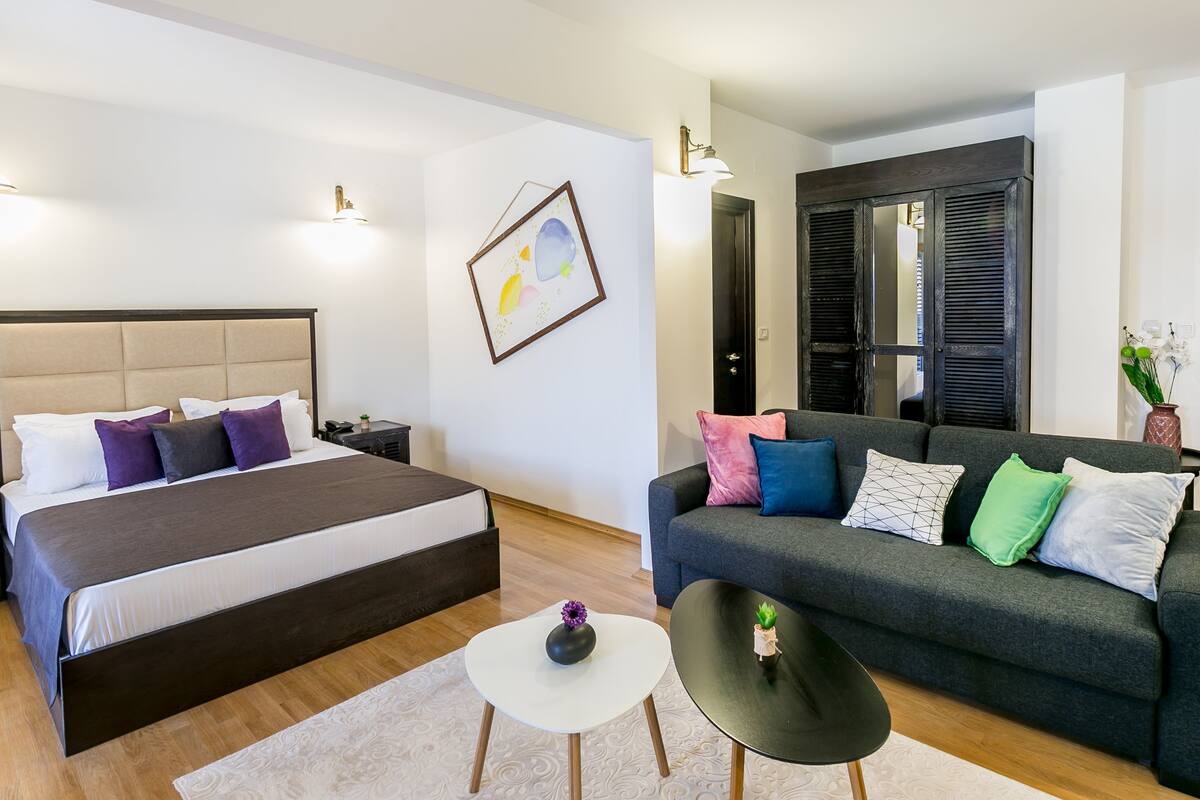 Ein modernes Schlafzimmer mit einem großen Bett, einem grauen Sofa und einem kleinen Tisch mit einer Vase.