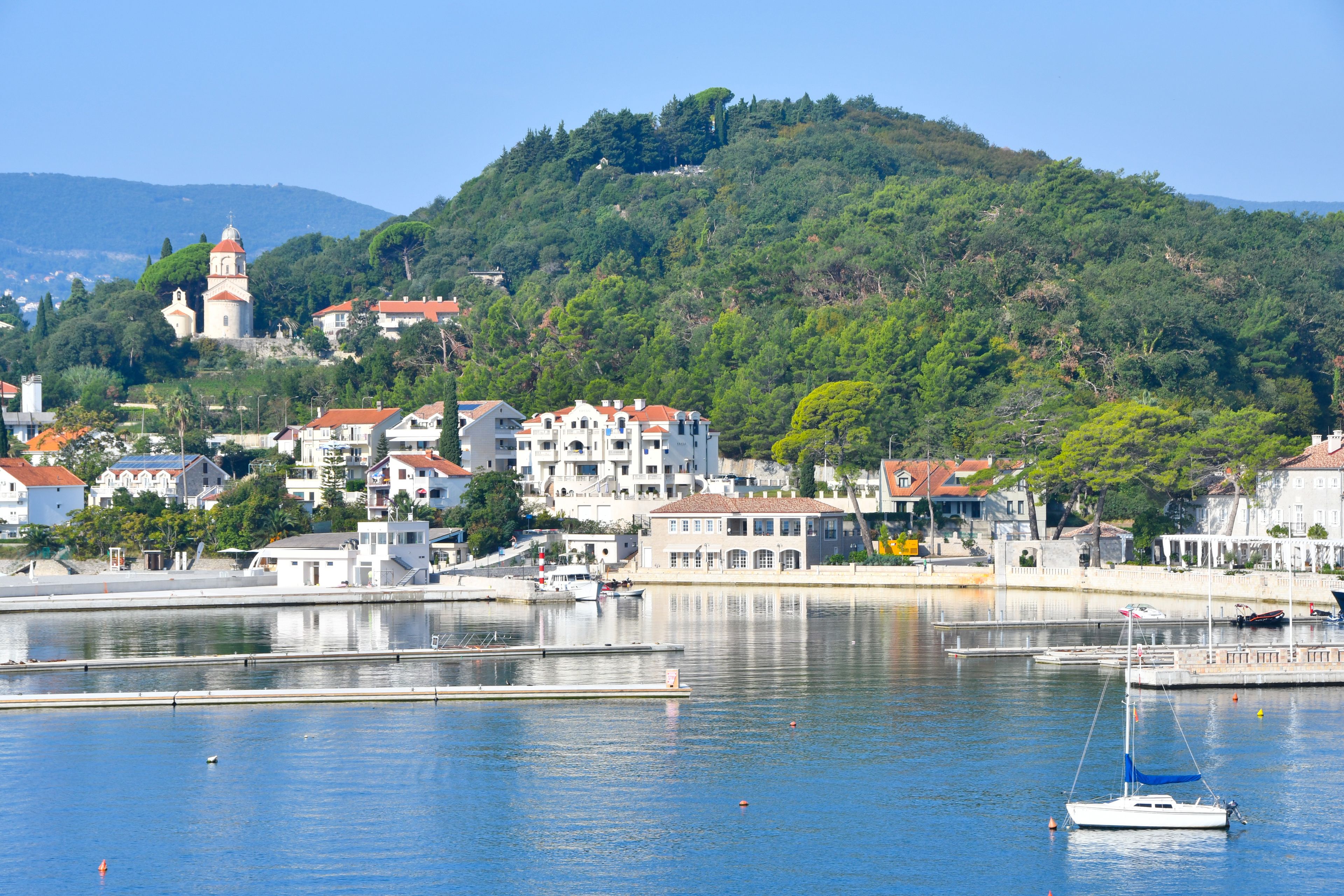 A coastal town with a prominent church on a hill, a marina with boats, and residential buildings along the waterfront.