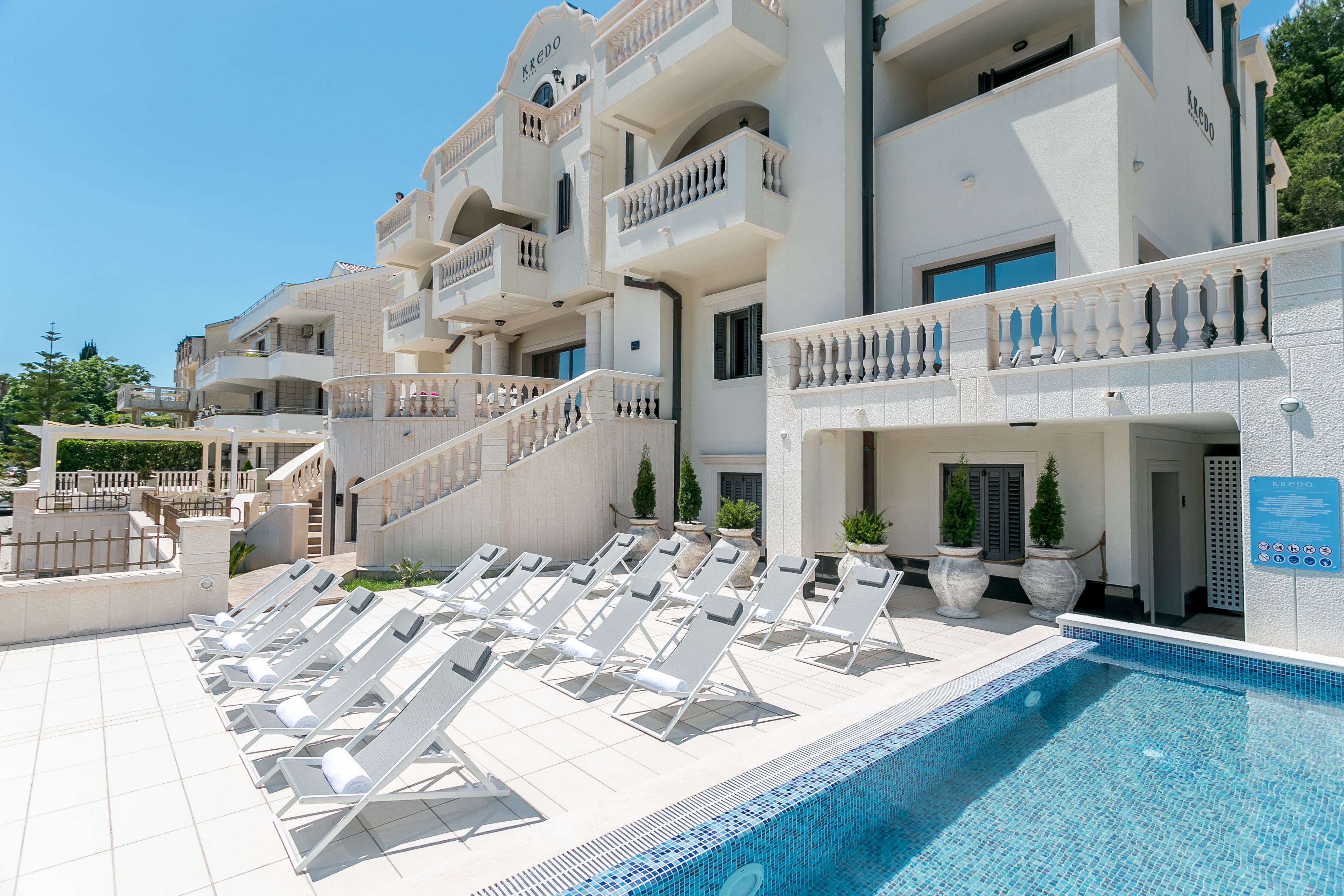 A hotel with a swimming pool, sun loungers, and a staircase leading to the upper floors.