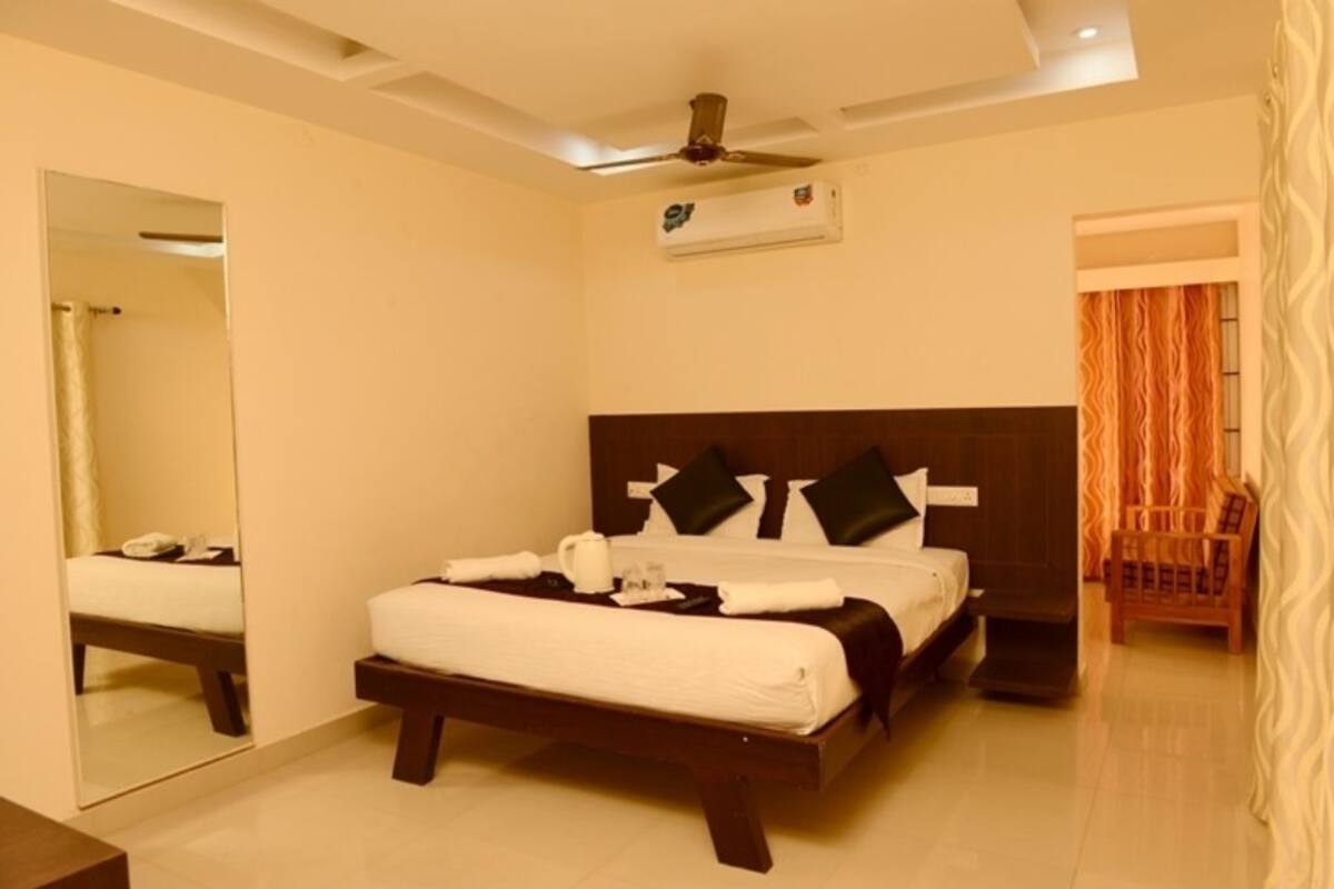 A bedroom with a bed, a ceiling fan, an air conditioning unit, a mirror, and a window with curtains.
