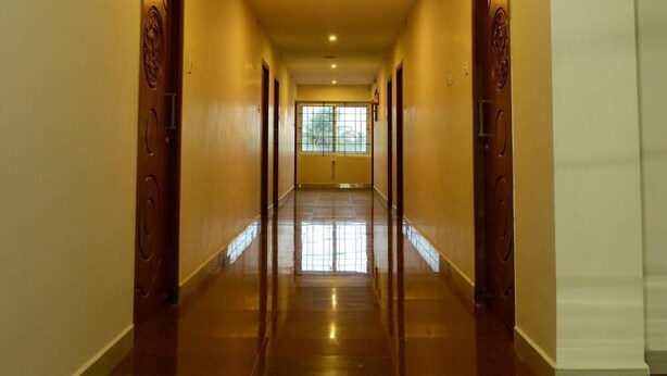 A long, narrow hallway with wooden doors on both sides and a tiled floor. - JK Residency (Tiruchirappalli)