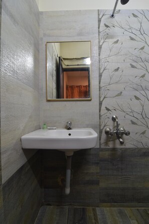 A bathroom with a white sink, a mirror, and a shower with a tree-patterned wall.