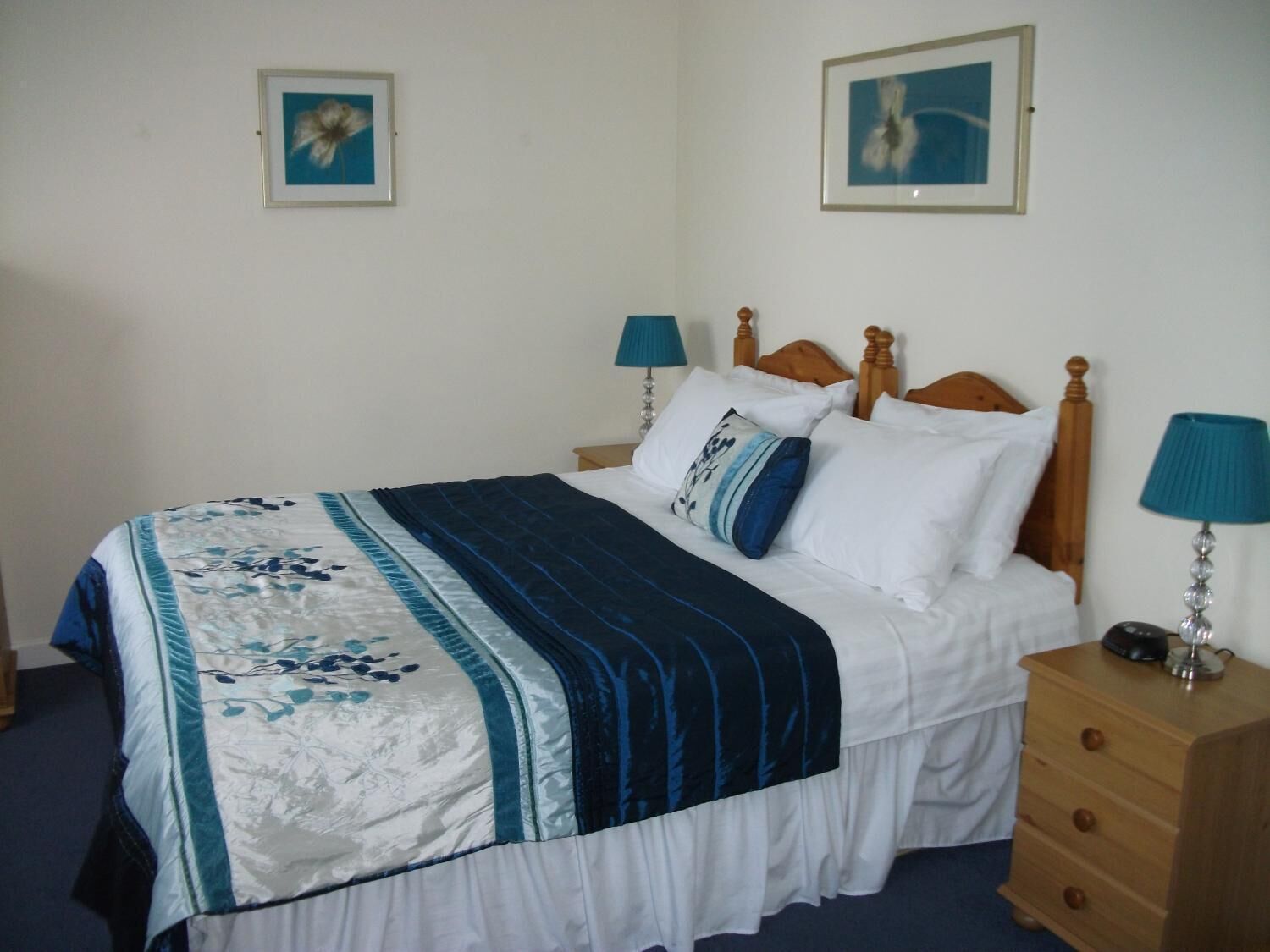 A neatly made bed with a floral bedspread, two bedside lamps, and a wooden nightstand with a lamp.