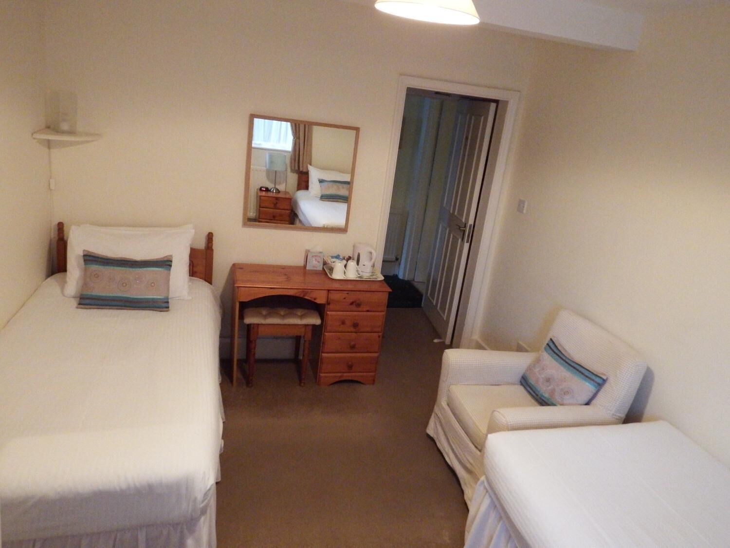 A small, clean room with two single beds, a wooden desk, a chair, and a mirror.