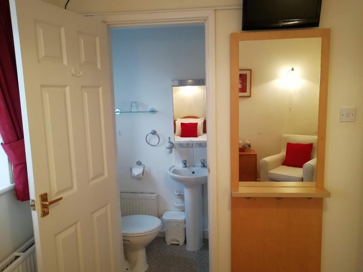 A compact bathroom with a toilet, sink, and shower. A mirror with a red pillow is visible.