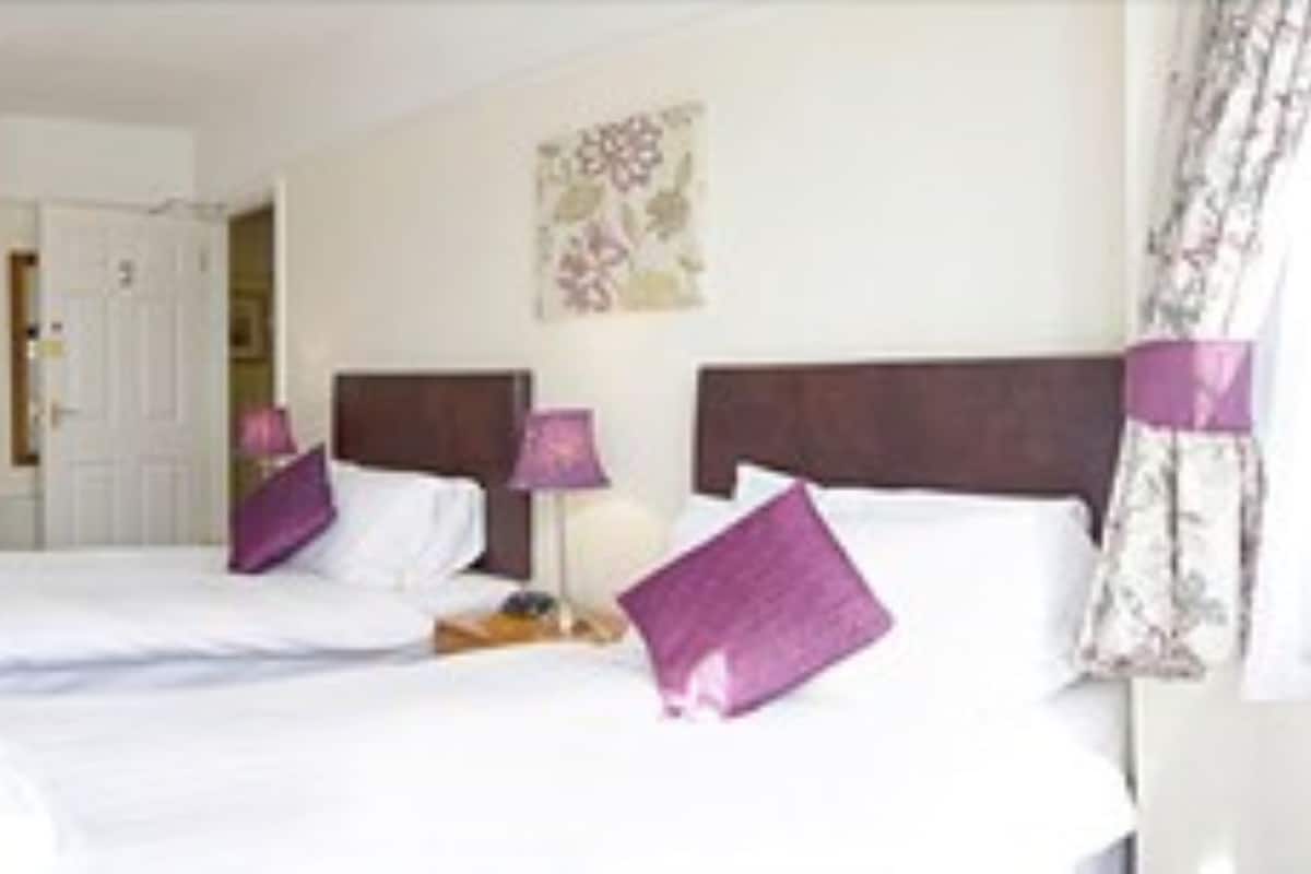 Quarto de hotel com duas camas, uma escrivaninha e uma cadeira.