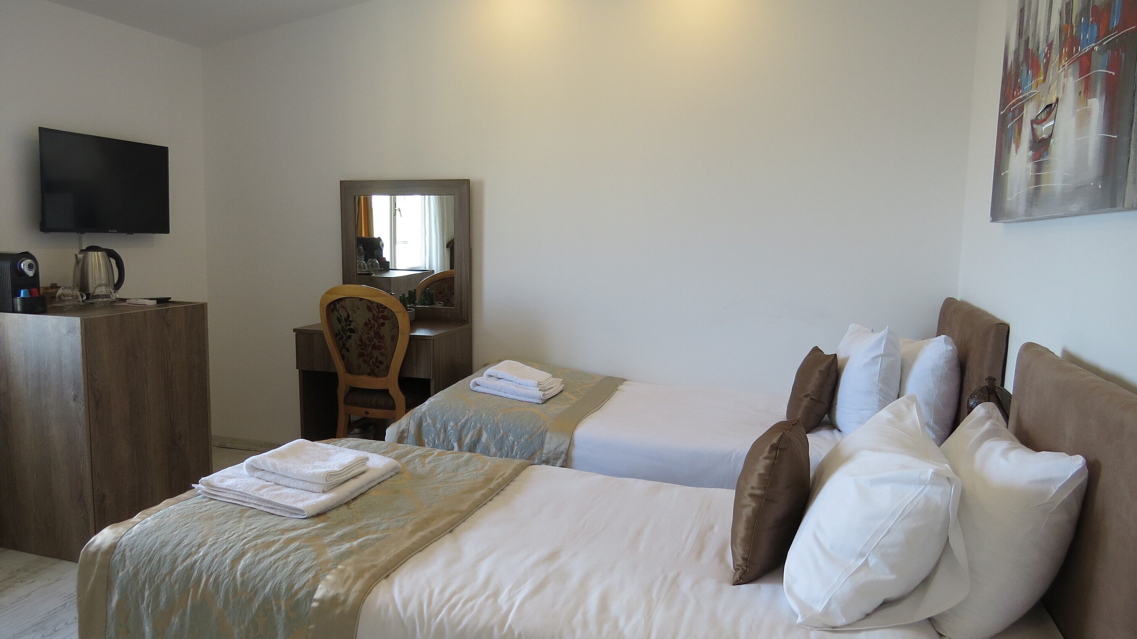 A hotel room with two beds, a desk, a chair, a television, and a painting on the wall.