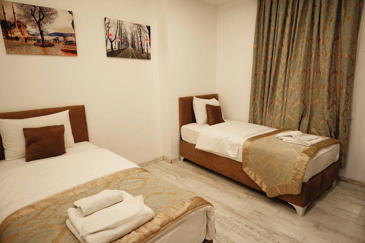 A hotel room with two beds, a large window with curtains, and artwork on the walls.