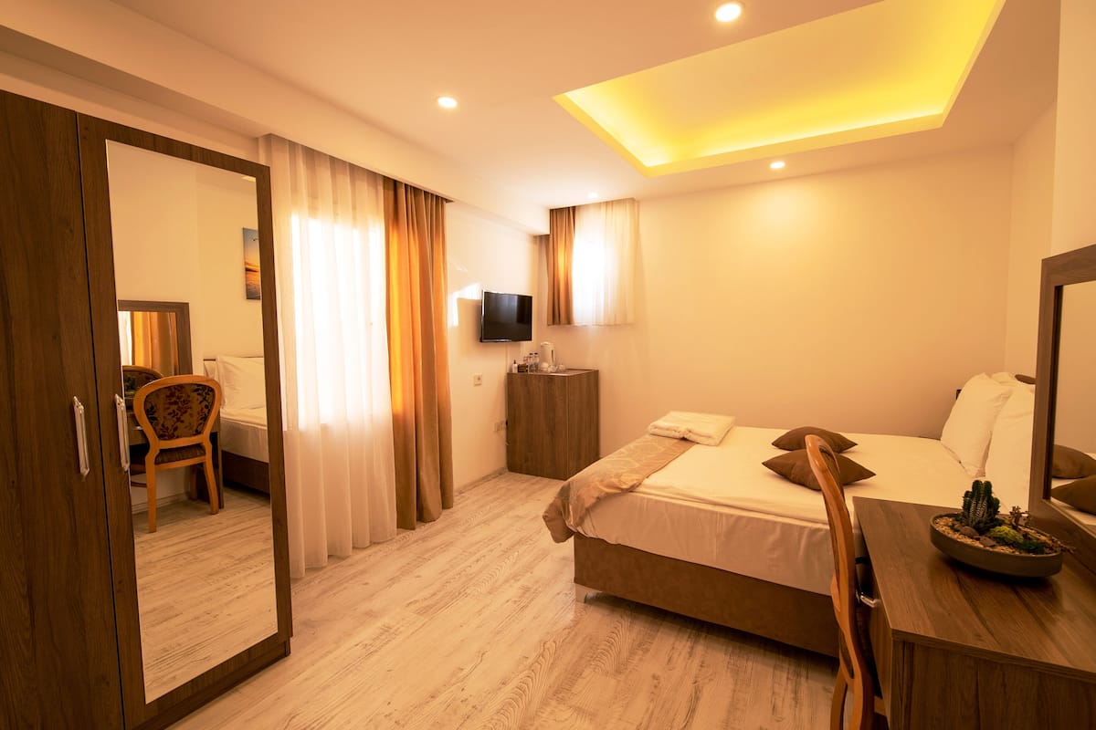 A hotel room with a bed, a wooden dresser, a mirror, a television, and a chair.
