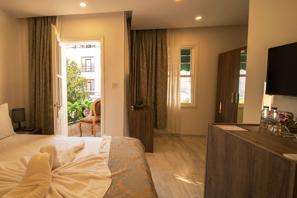 A hotel room with a bed, a desk with a flat-screen TV, a chair, and a view of the outside balcony.
