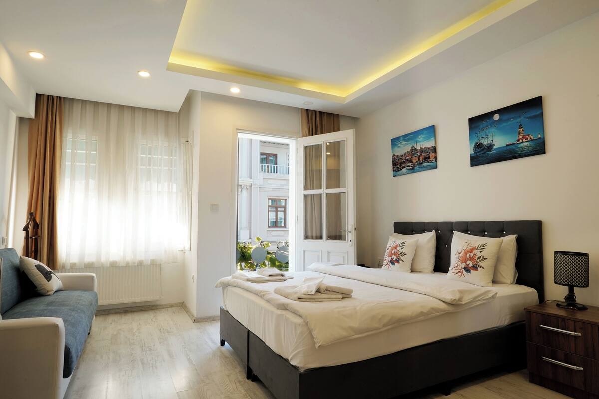 A modern bedroom with a bed, bedside table, and a view through an open door to the outside.