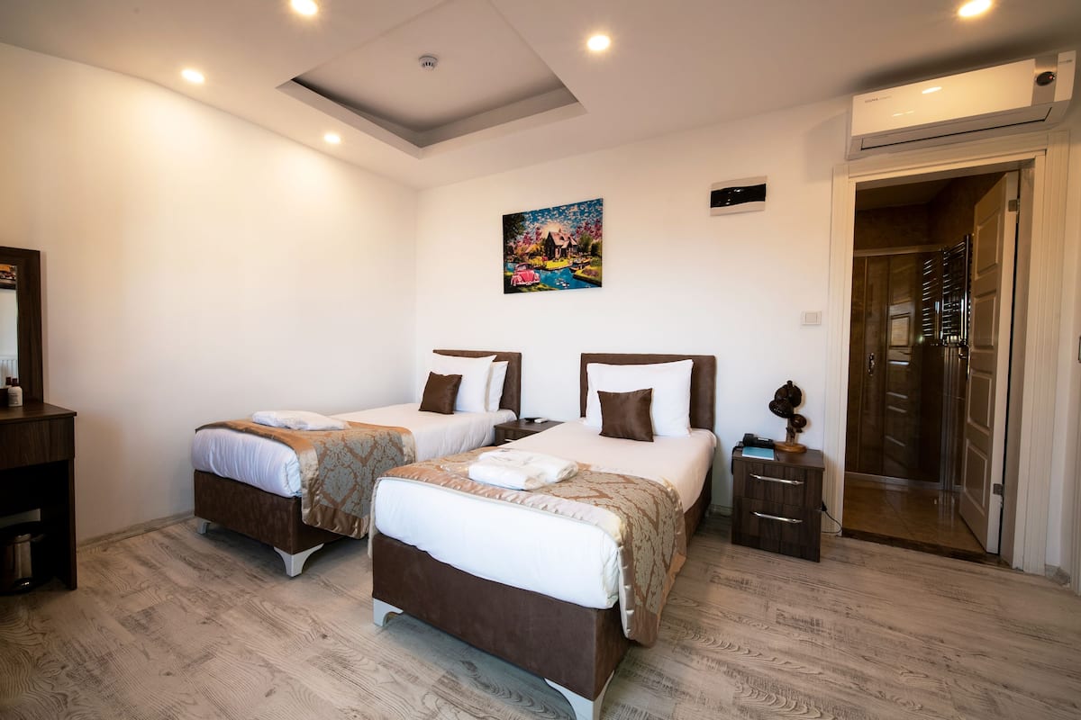 A hotel room with two beds, a desk, a chair, a painting on the wall, and a door leading to a bathroom.