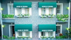 Fachada de edificio con cuatro ventanas, cada una con un toldo verde y contraventanas blancas, que dice "HOUSE OF ZEUGMA".