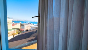 Vista a través de una ventana con manija metálica, que da a una calle con edificios y un cuerpo de agua a lo lejos.