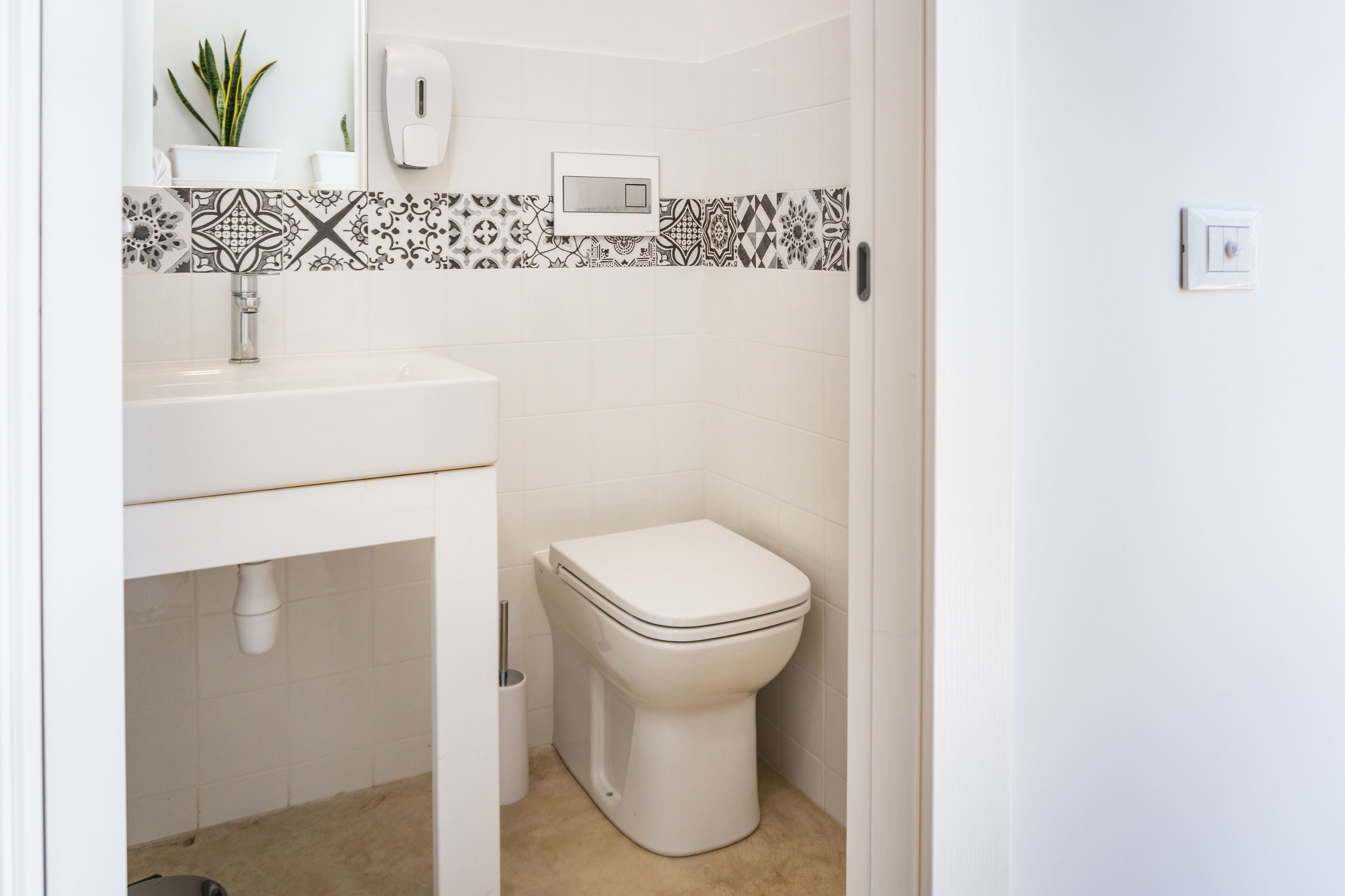 A bathroom with a white sink, a toilet, and patterned tiles on the wall.