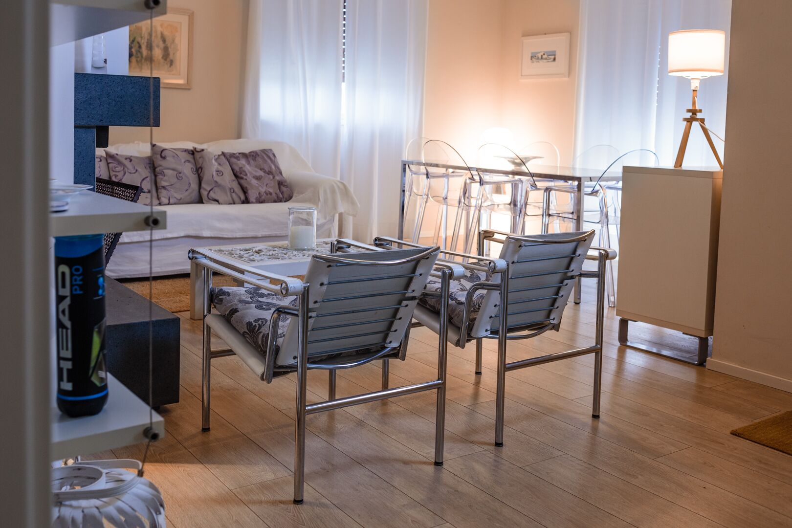 Ein modernes Wohnzimmer mit einer Couch, einem Esstisch mit Glasplatte und Metallstühlen.