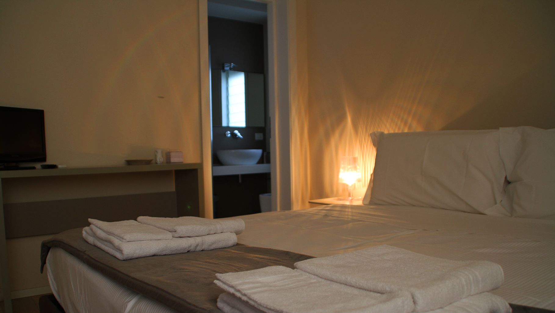 Una habitación de hotel con cama, televisor, lavamanos y espejo.