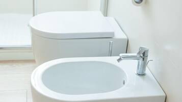 Une salle de bain équipée de toilettes, d’un lavabo et d’un porte-rouleau de papier toilette fixé au mur.