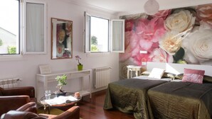 Une chambre avec deux lits, un radiateur, un bureau avec une chaise, une fenêtre avec des rideaux et une fresque florale sur le mur.