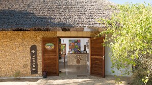 Un bâtiment rustique avec un toit de chaume et des murs en pierre, doté d’une porte en bois et d’une enseigne sur laquelle on peut lire « billets ».