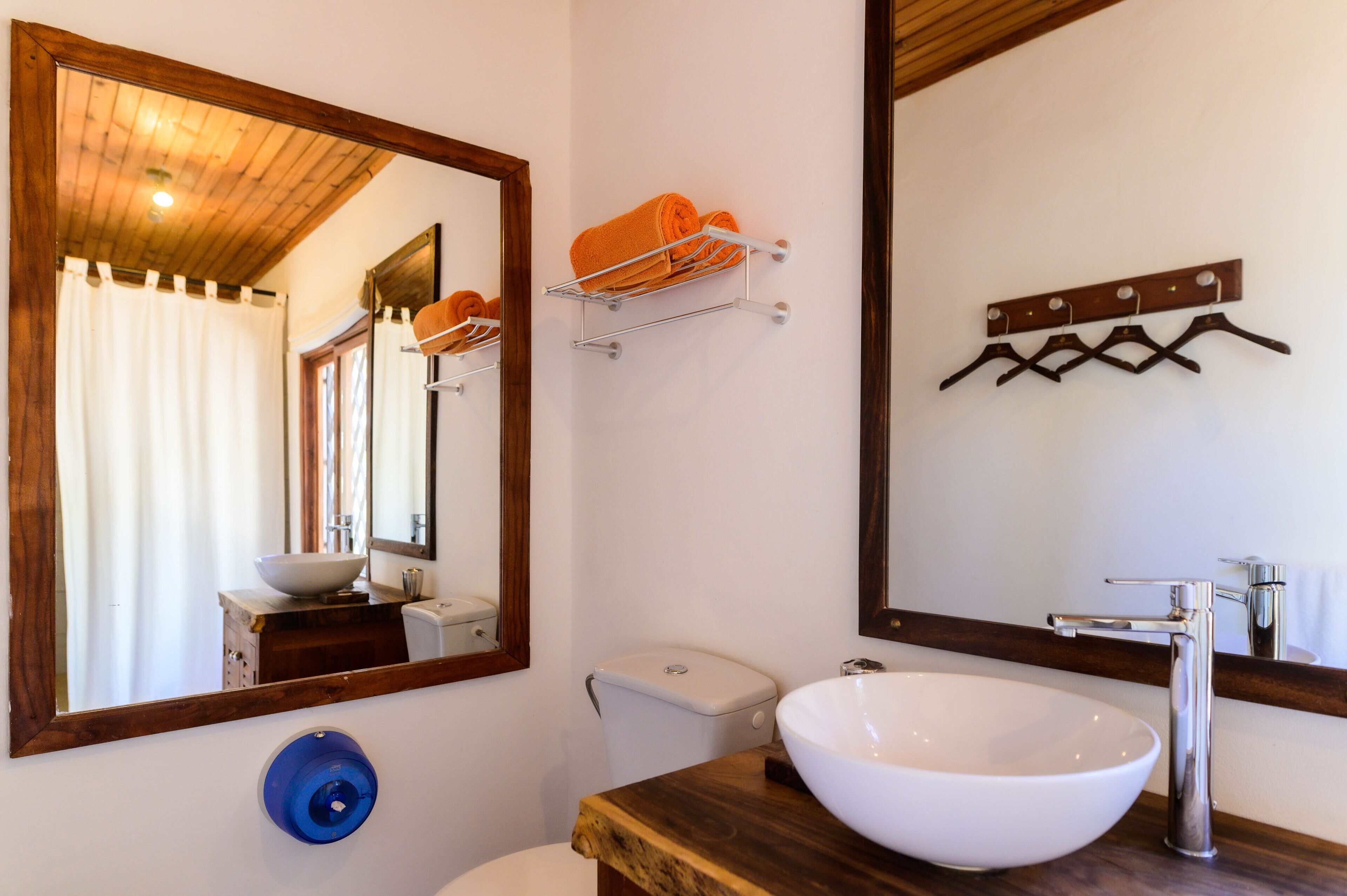 Un baño con tocador de madera, un lavamanos blanco, un espejo y un perchero con toallas.