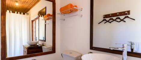 Un baño con tocador de madera, un lavamanos blanco, un espejo y un perchero con toallas.