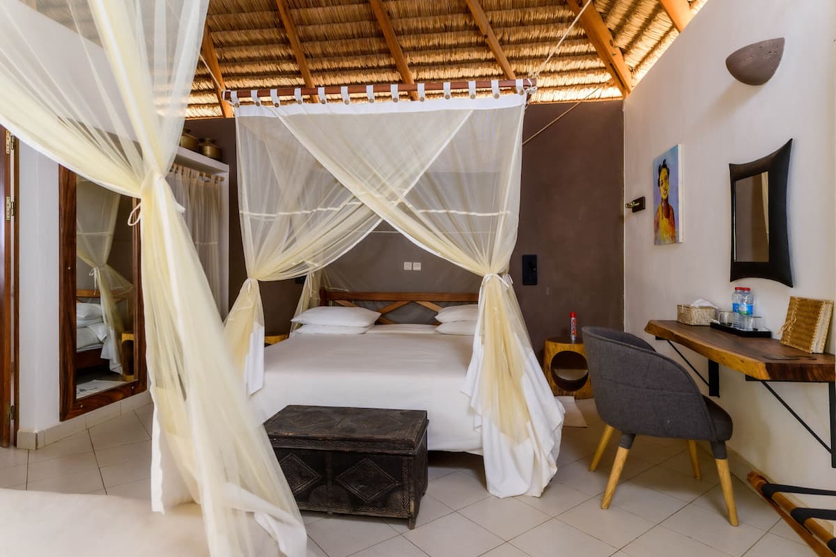 A room with a bed under a canopy, a desk with a chair, and a small table with a lamp.