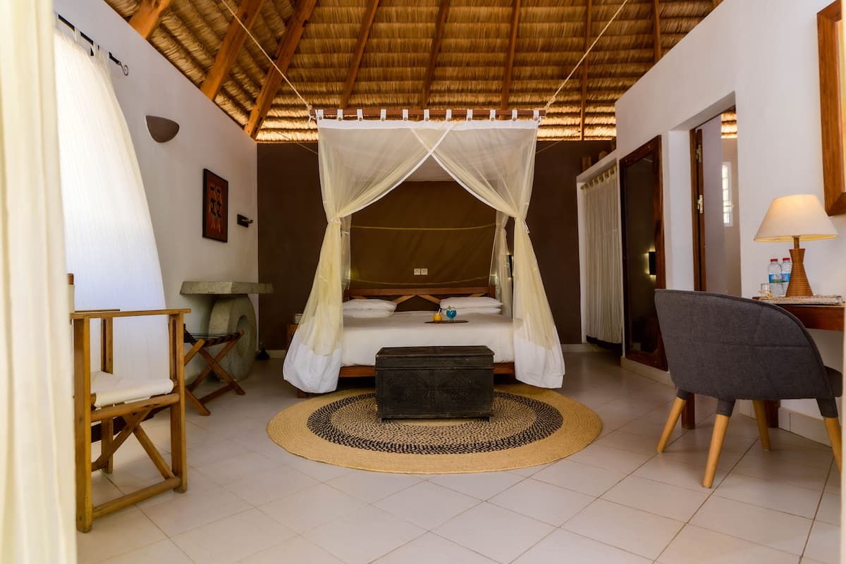 A room with a bed under a canopy, a desk with a lamp, and a chair.