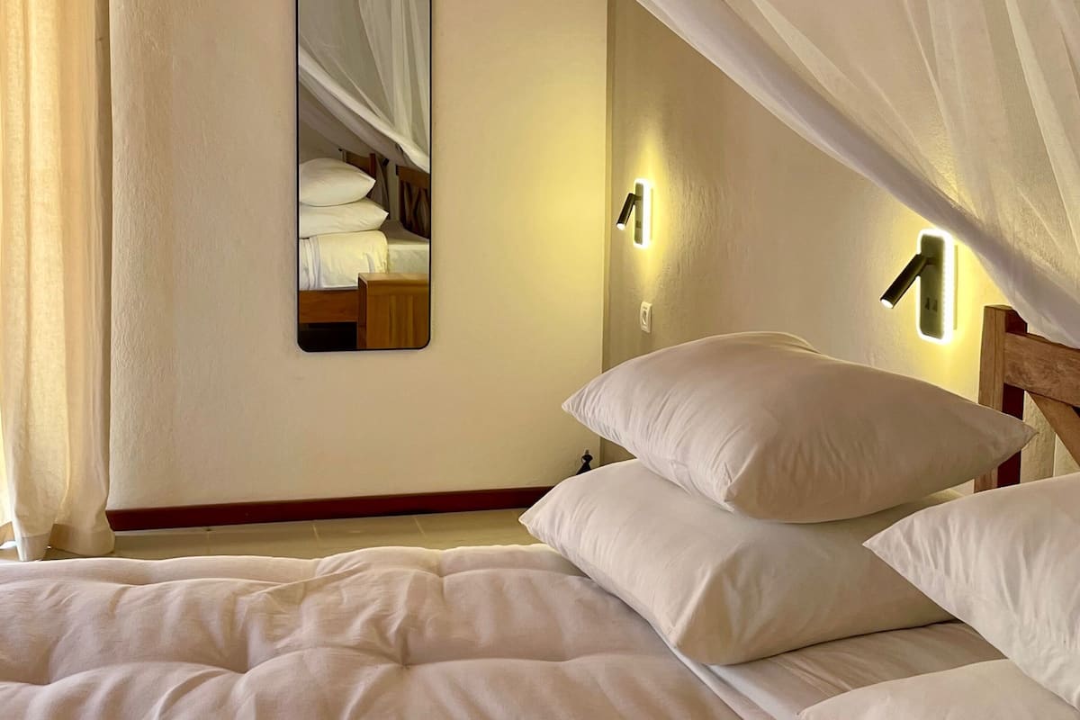 A bedroom with a canopy bed, a bedside mirror, and wall-mounted lights.