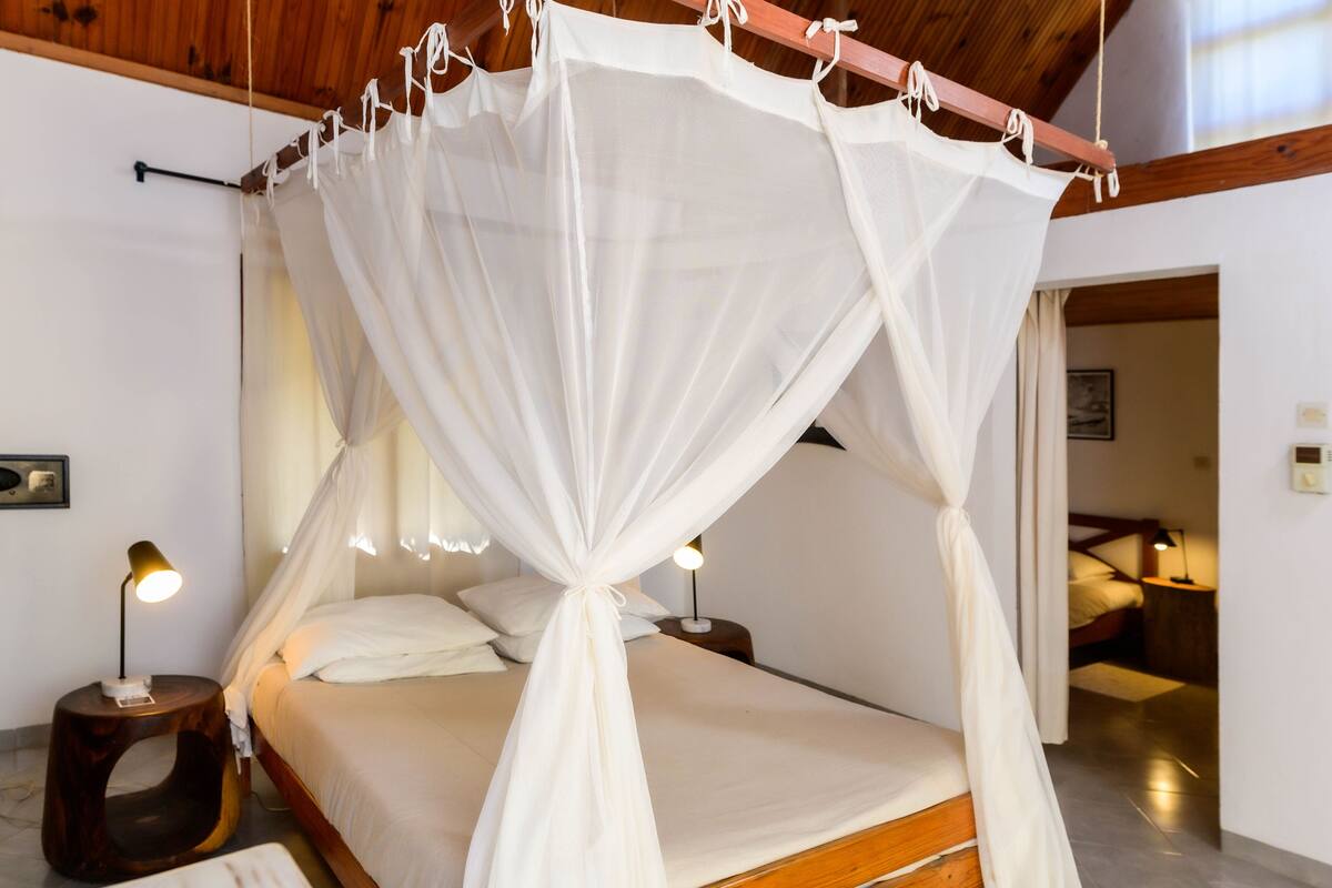 A bedroom with a canopy bed, bedside lamps, and a wooden headboard.