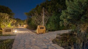 Un chemin de pierre mène à un bungalow portant l’inscription « bungalow 7 », avec des panneaux indicateurs et un éclairage abondant.
