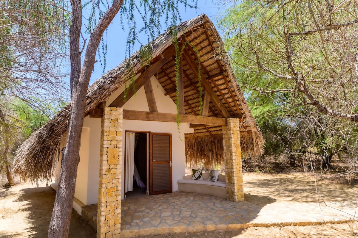 A small, rustic hut with a thatched roof, a wooden door, and a stone-paved entrance area.