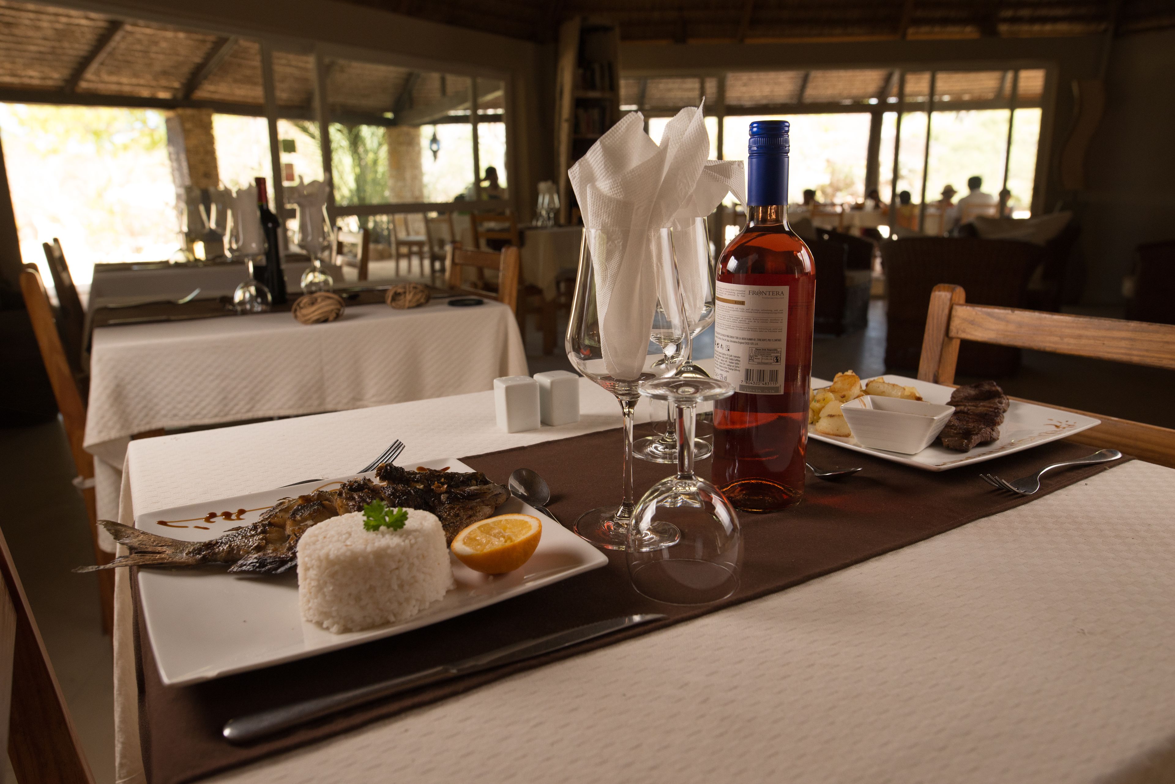 A dining table set with a plate of food, a bottle of wine, and a glass.