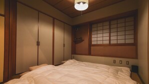 Un dormitorio japonés tradicional con una cama grande, puertas correderas y una ventana con celosía de papel.