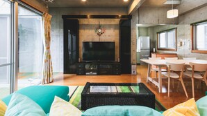 Una sala de estar moderna con un televisor de pantalla plana, un comedor con sillas blancas y una cocina al fondo.