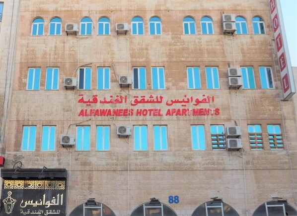 A building with multiple windows and air conditioning units. The text on the building reads "ALFAWEES HOTEL APARTMENTS".