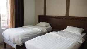 A room with two single beds, wooden headboards, and a large window with curtains.