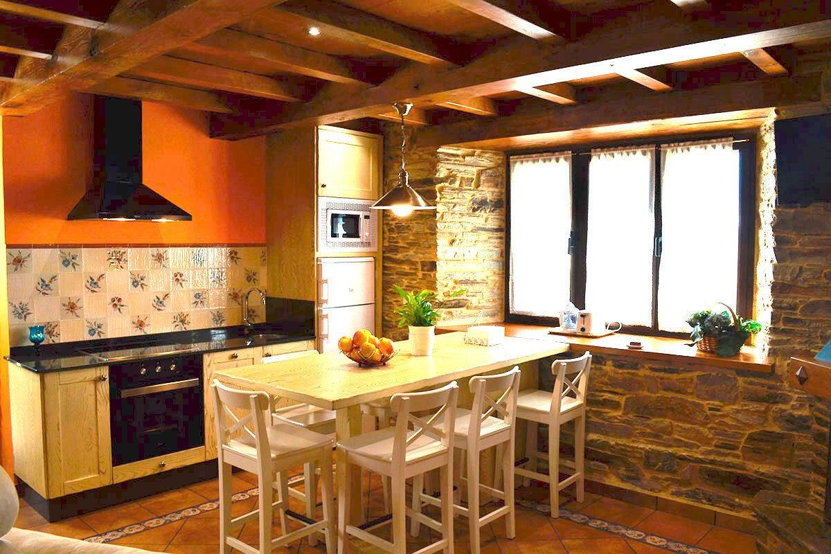 A kitchen with a wooden island, white chairs, a stone wall, and a window with curtains.
