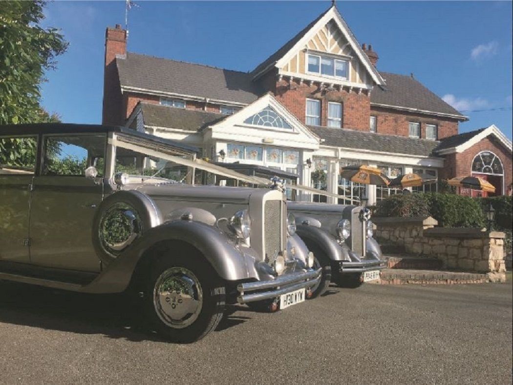 A vintage car parked in front of a large, traditional house with a prominent gabled roof and a large windowed porch.