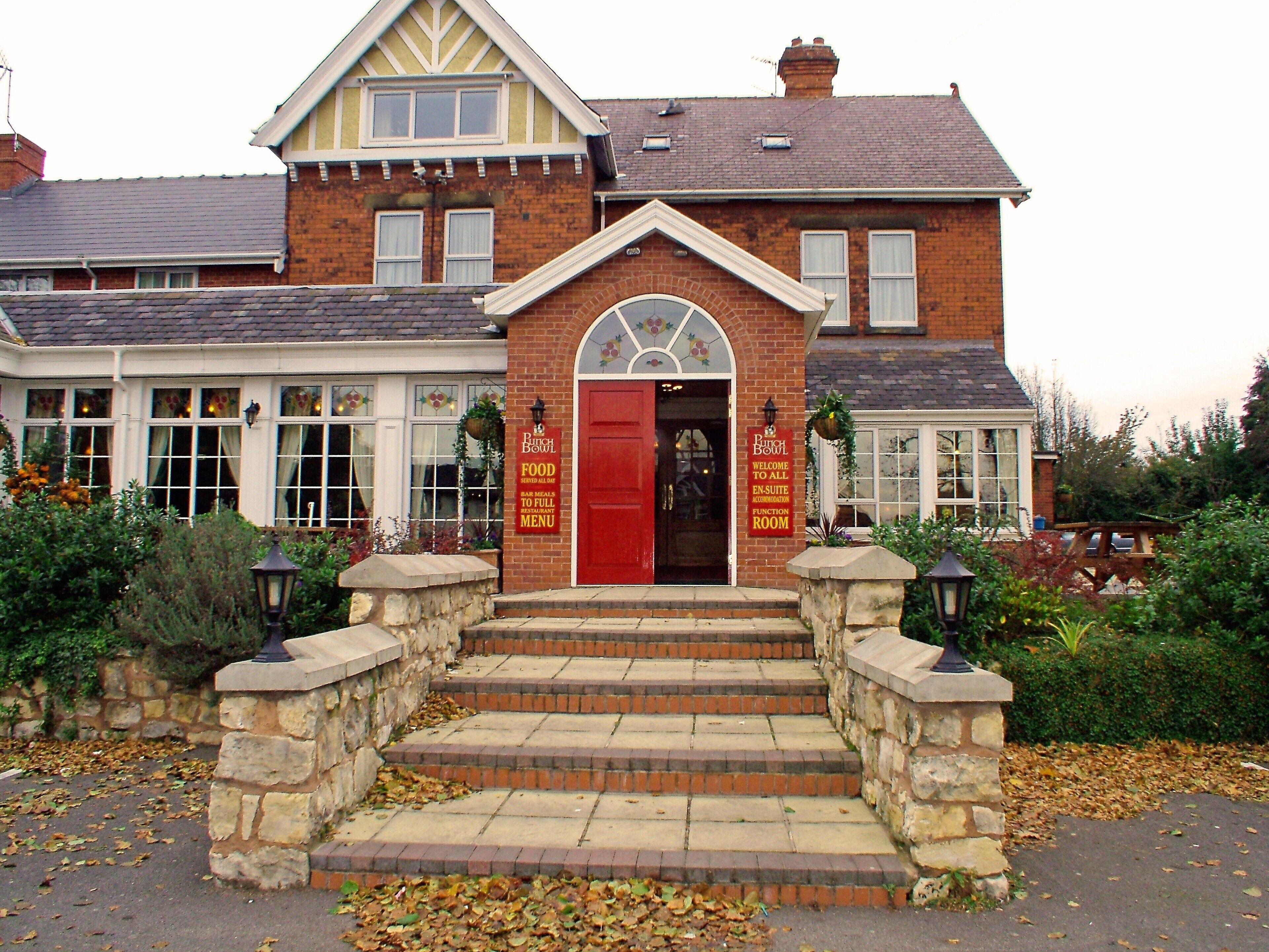 A two-story building with a red entrance door, stone steps, and a sign indicating it is a restaurant.