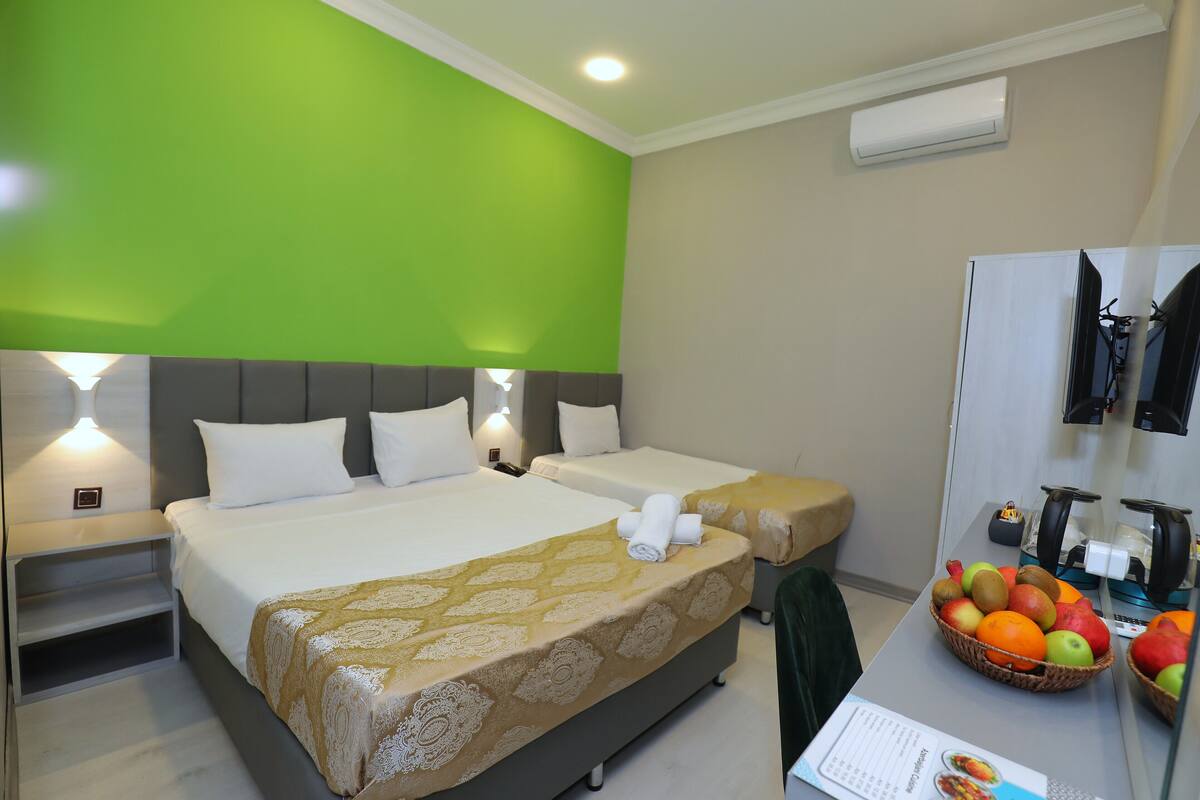 A hotel room with two beds, a desk with a fruit basket, and a mirror.
