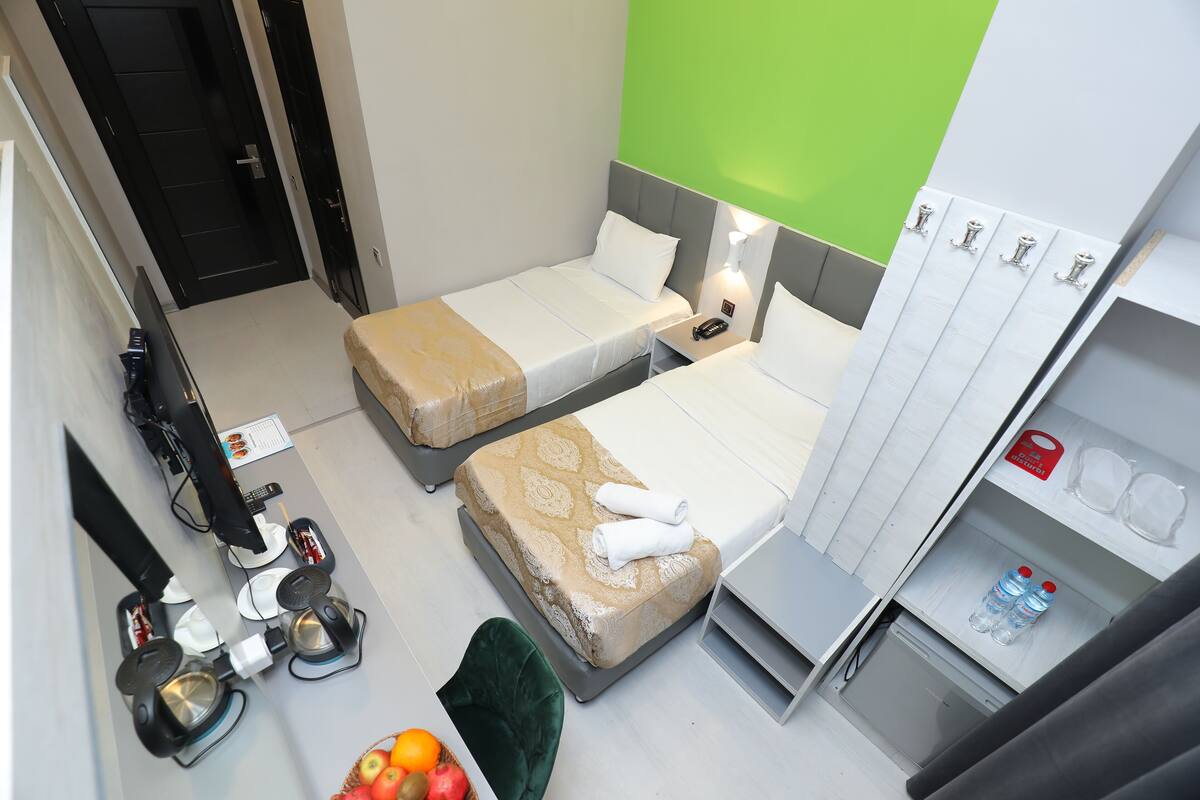 A hotel room with two single beds, a desk with a chair, a small refrigerator, and a minibar.