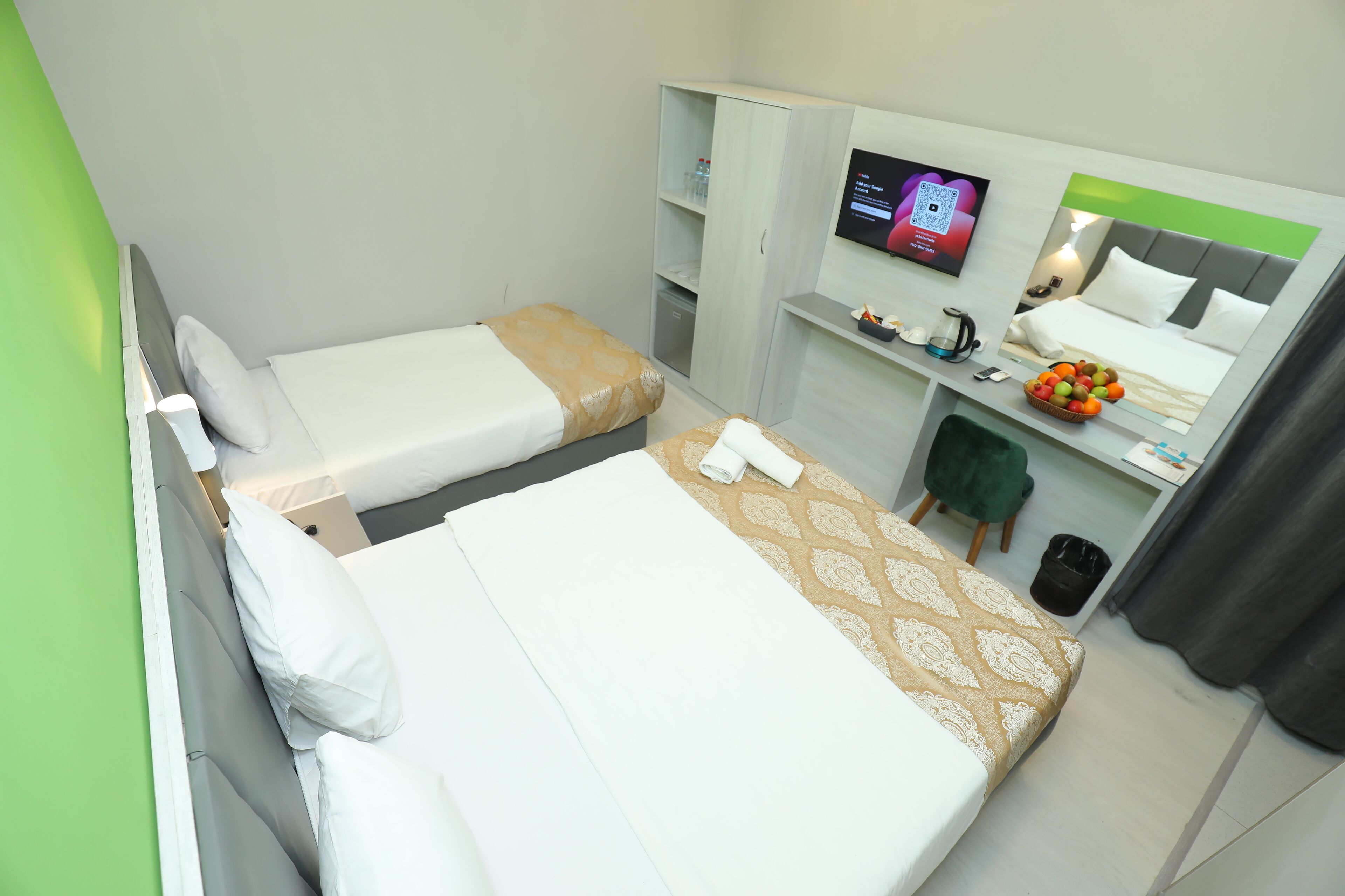 A hotel room with two beds, a TV, a desk with a computer, and a small seating area.