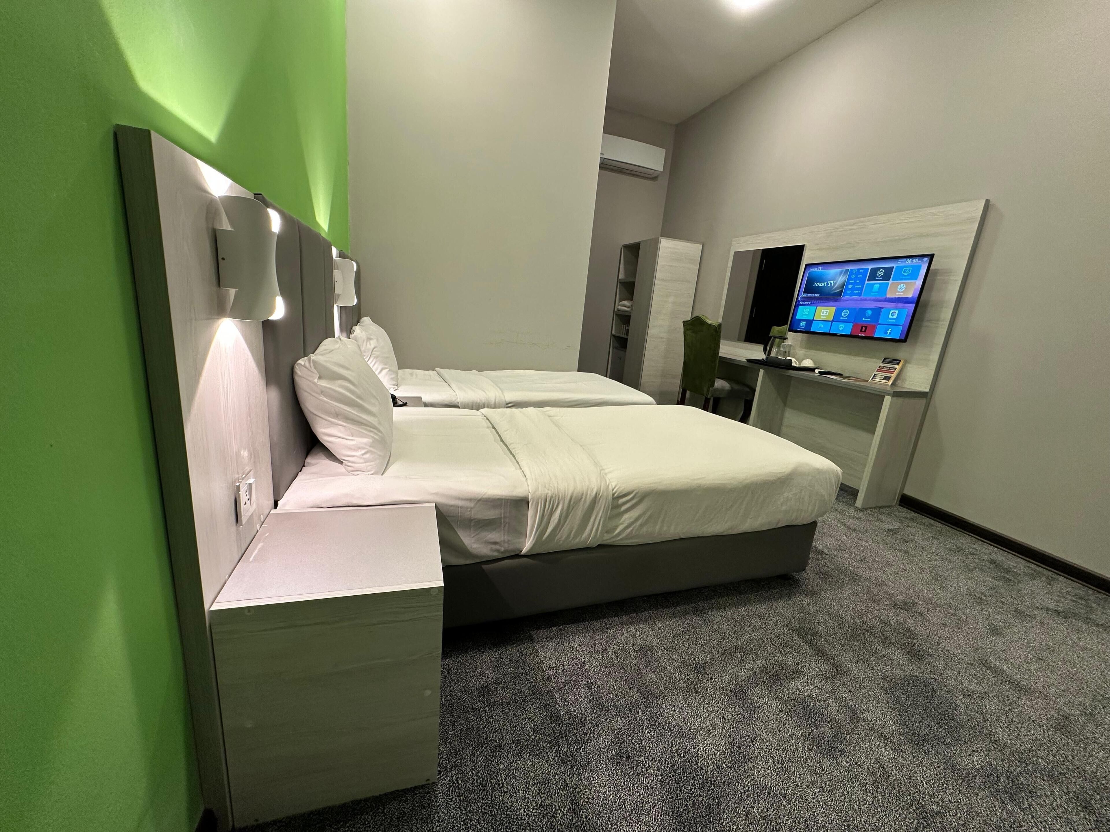 Habitación de hotel moderna con cama doble, mesita de noche, televisor y una pared verde de acento.