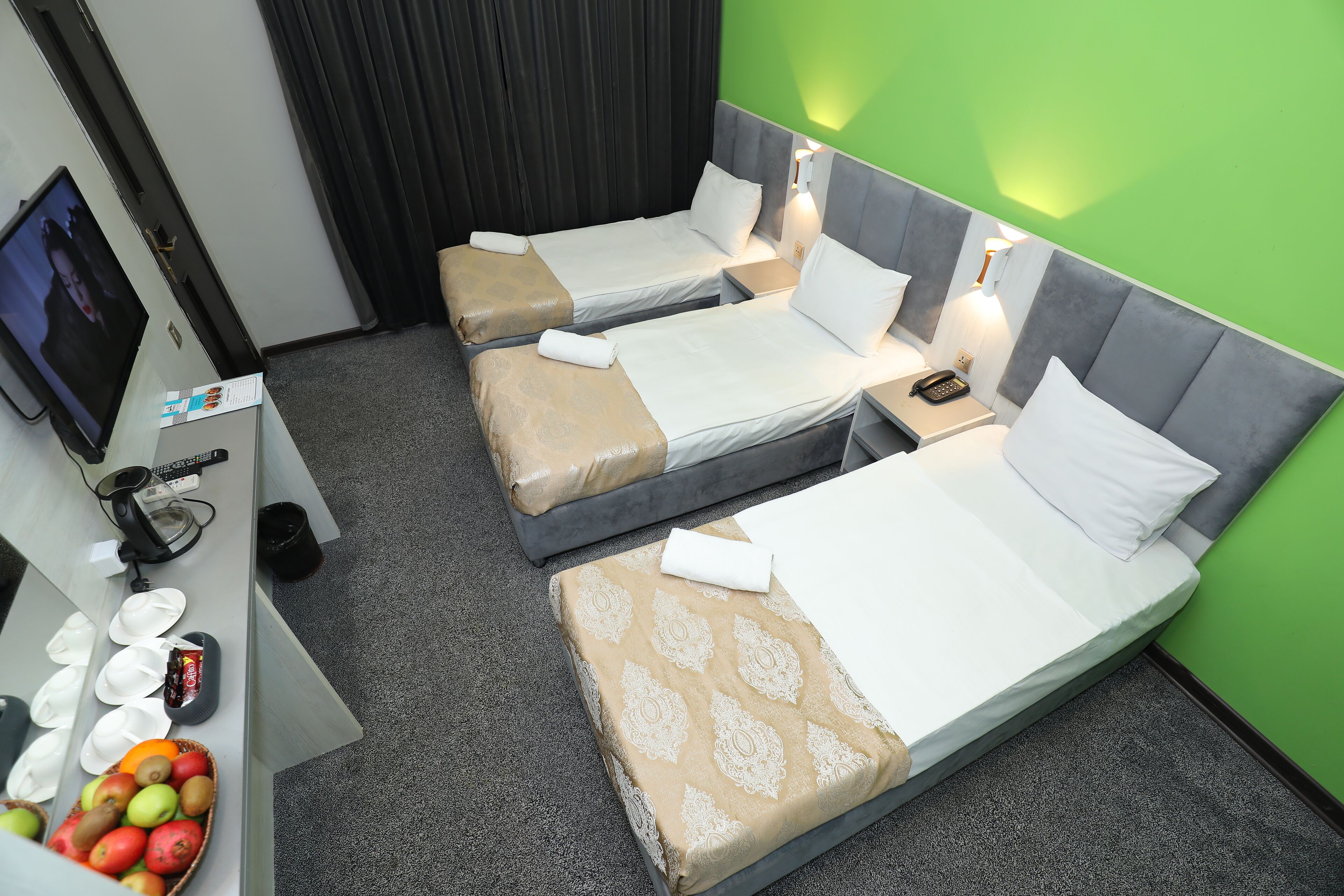A hotel room with two beds, a desk with a computer, a TV, and a fruit basket.