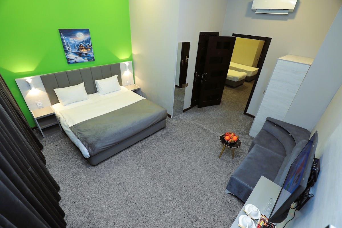 A hotel room with a bed, bedside tables, a desk with a chair, a wardrobe, and a painting on the wall.