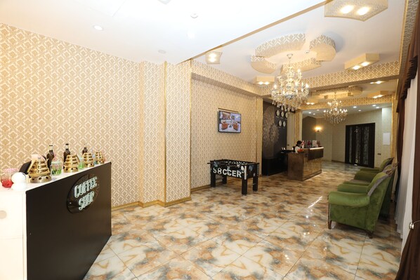 A lobby with patterned wallpaper, a coffee shop counter, a soccer-themed bench, a reception desk, and a green sofa. - İstanbul Gold Hotel Baku (Baku)
