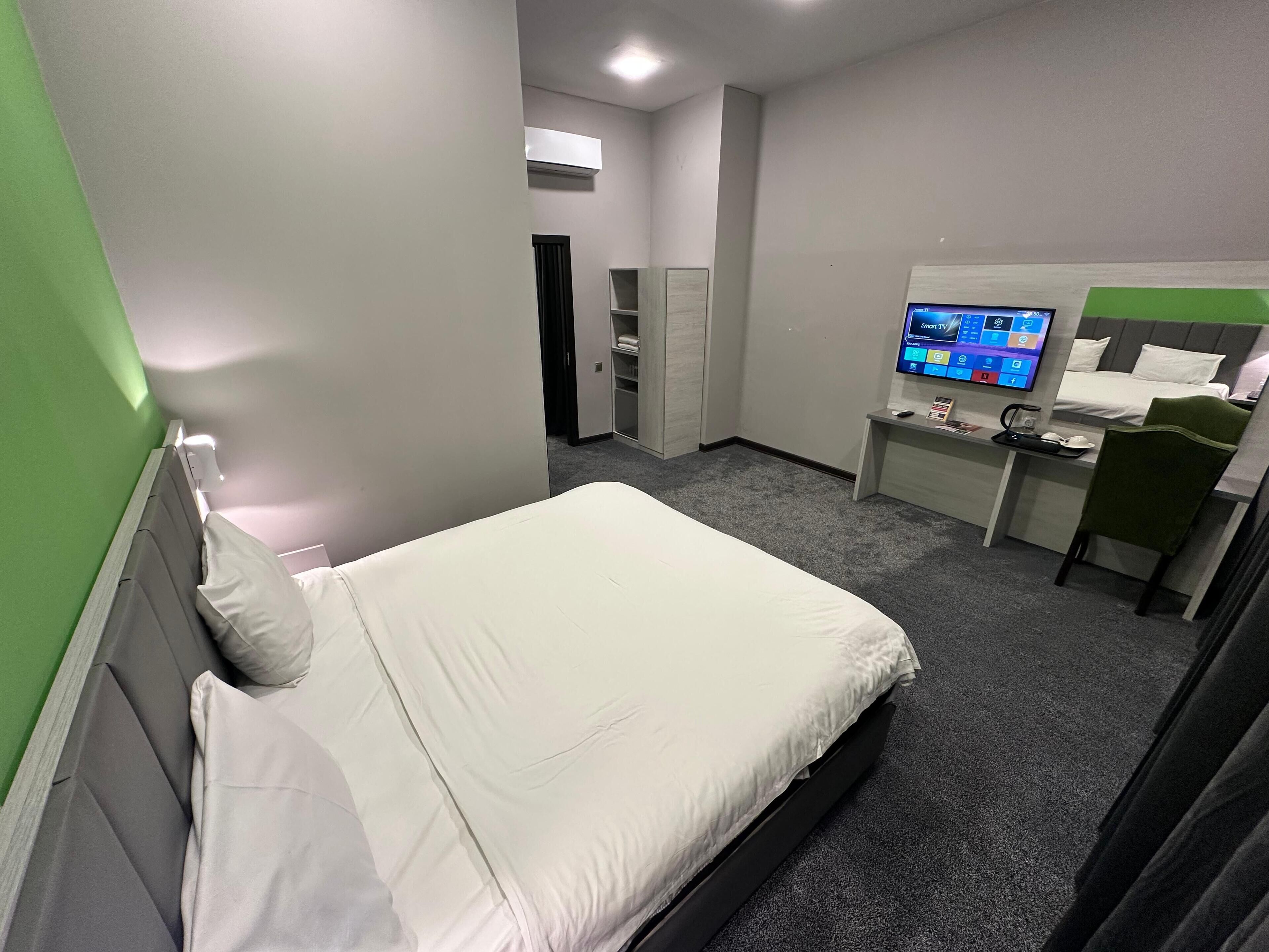 A hotel room with a bed, a desk with a computer, a TV, and a wardrobe.