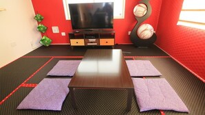 A room with a TV, a wooden table, and purple mats on the floor. - Guest House Rion (Yomitan)