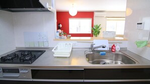 A kitchen with a gas stove, stainless steel sink, and a window with a view. - Guest House Rion (Yomitan)